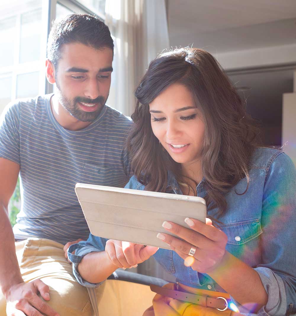 Two people sitting together in warm natural light, looking at a tablet.